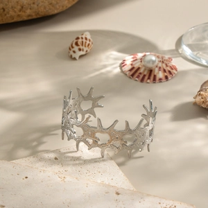 Detailed view of silver heart-shaped thorn bangle on a stone surface with pearls