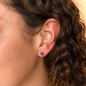 Close-up of heart-shaped blue zircon stud earrings on model with rose gold finish