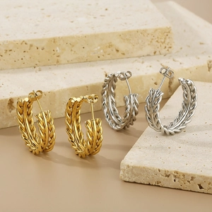 Chic twisted C-shaped hoop earrings in gold and silver finish on a stone pedestal