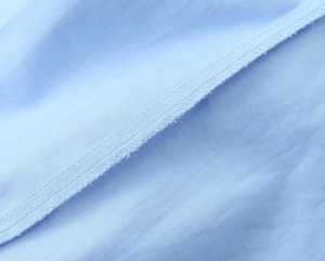 Makro-Detail der feinen Nähte und der hellblauen Stoffstruktur auf dem Hemd mit Schulterpolstern