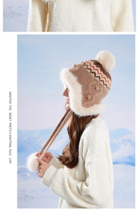 Close-up of brown knit hat with faux fur lining and large pompom against snow mountains