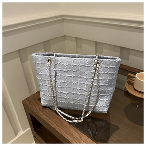 Detail of light blue tweed tote bag with golden chain strap on a wooden table