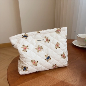 Close-up of quilted bear print makeup bag with a minimalist white label on a wooden desk