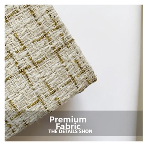 Close-up of premium tweed fabric with ivory woven texture and metallic gold thread details