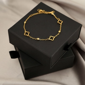 Elegant gold titanium steel bracelet featuring four hollow clover charms on grey silk