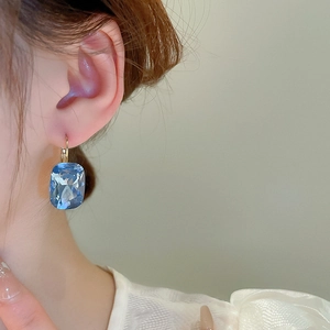 Close-up of light blue rectangular gemstone earrings with gold hooks and diamond accents