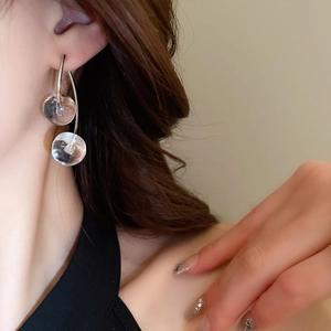 Macro shot of silver drop earrings with transparent glass beads on a model's ear