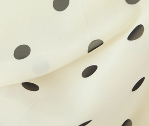 Macro shot of black polka dots on cream chiffon fabric showing soft drape and texture