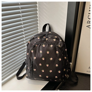 Close-up of black nylon mini backpack featuring pink floral prints and front zipper pocket