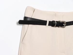 Detail of black faux leather belt with silver metal buckle on beige trousers