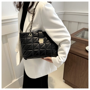 Detail of black quilted shoulder bag with gold chain strap and metal lock closure