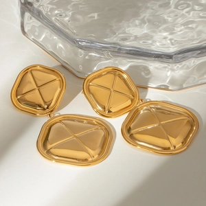 Detailed close-up of chunky gold earrings with square geometric shape and cross texture