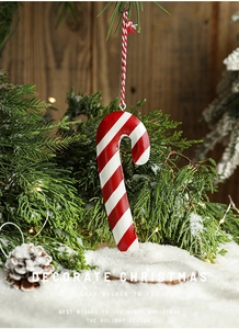 Detailed view of metal candy cane ornament hanging on a snowy Christmas tree branch