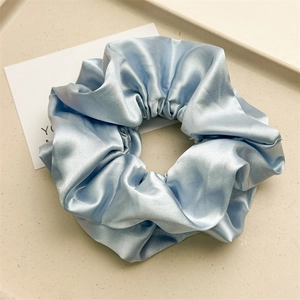 Detail view of a large light blue pleated satin scrunchie on a textured beige tray