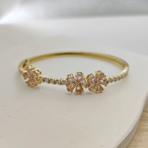 Detailed shot of golden open bangle featuring pink clover flowers and sparkling white zircons