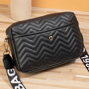 Detail of black V-quilted leather bag with golden clasp and wide branded shoulder strap