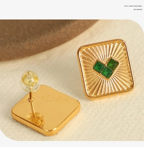 Detail of square gold stud earrings with green heart-shaped zircons on stone background