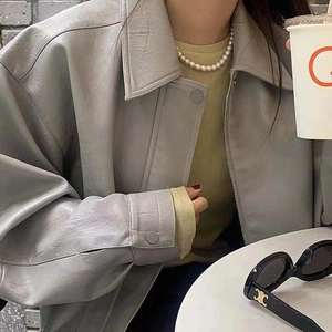 Detailed view of an elegant pearl necklace paired with a chic grey leather jacket