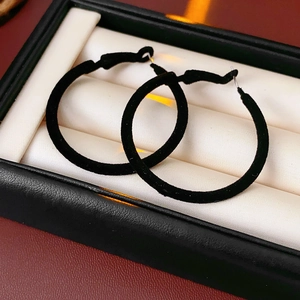 Detailed close-up of black velvet flocked hoop earrings on a soft jewelry cushion