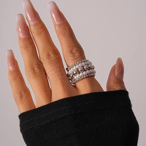 Detail of layered faux pearl and silver beaded elastic rings worn on a hand model