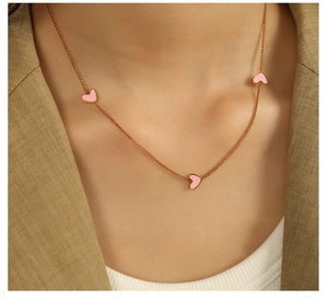 Close-up of a gold necklace with three pink heart pendants worn by a female model