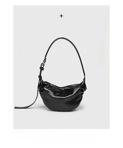 Detail shot of black glossy pleated crescent bag with adjustable buckle strap and texture