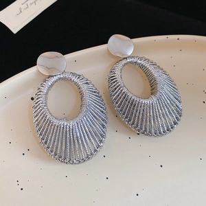 Gros plan de boucles d'oreilles ovales en fil tissé sur une assiette en céramique crème