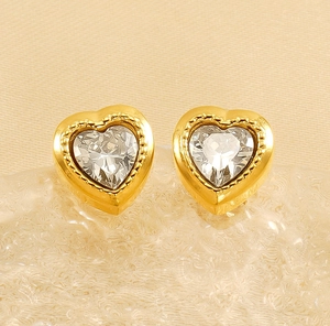 Close-up of heart-shaped gold earrings with clear zircon stones and milgrain texture