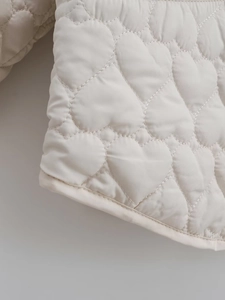 Close-up of heart-shaped quilting pattern on off-white padded cotton jacket fabric