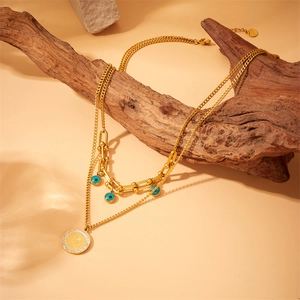 Gold layered stainless steel necklace with blue evil eye bead and coin pendant on wood