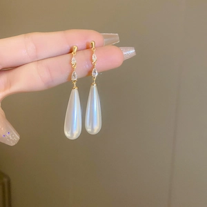 Close-up of gold pear-shaped crystal earrings with elegant white teardrop pearl pendants