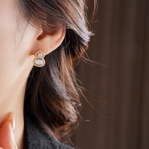 Macro shot of gold-plated gourd stud earrings with zircon stones on model's ear