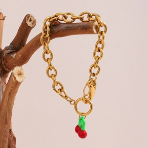 Detail of gold chain bracelet hanging on wooden branch with red and green cherry charms