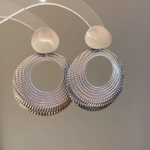 Gros plan détaillé de grandes créoles argentées avec une texture tissée complexe