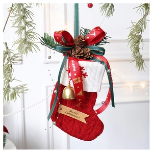 Detail of red knitted Christmas stocking with large ribbon bow, pine cones and golden bell
