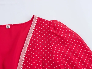 Dettaglio macro dello scollo a V con perle finte su un abito rosso a pois bianchi