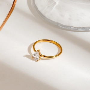 Close-up of gold stainless steel ring featuring a pear-cut clear gemstone on a display