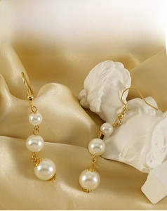 Détail de boucles d'oreilles en or 18 carats avec trois perles graduées sur soie dorée