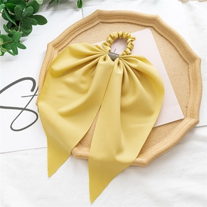 Detail of yellow satin bow hair scrunchie with rhinestone buckle on wooden tray