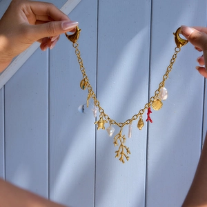 Gold-plated ocean charm bracelet with turtles and pearls shown on a hand against blue wood