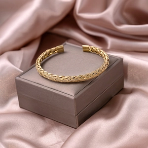Macro shot of gold woven cuff bracelet with intricate metal textures on a pink silk background