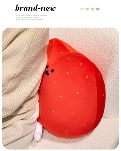 Detail of red strawberry plush pillow with embroidered seeds on a white textured sofa