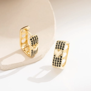 Goldene Herz-Ohrringe mit schwarzen Schmucksteinen auf minimalistischem Steinhintergrund