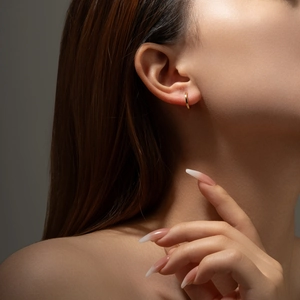 Close-up of minimalist gold-plated hoop earrings on a model with neutral studio lighting