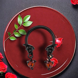 Black horseshoe nose ring with red heart gemstone and wings on a bed of red roses