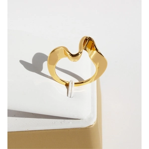 Minimalist irregular wave gold-plated brass ring on a white display stand