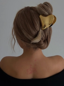 Detailed view of a golden metal heart-shaped hair claw clip on light brown hair