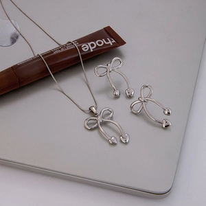 Silver bow necklace and earrings set with heart charms on a sleek metallic surface