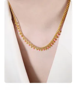 Detail of gold chain necklace with pink enamel and metal beads worn by a model