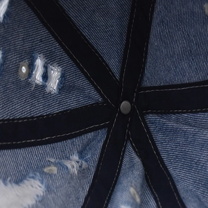 Macro view of distressed denim cap interior with reinforced black stitching and metal rivet